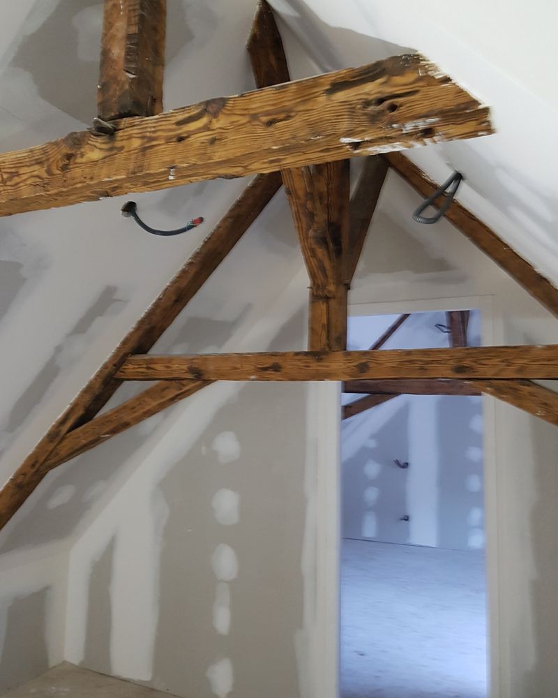 Combles aménagés : plaques de plâtre posées sous une charpente ancienne conservée, bandes et joints en cours