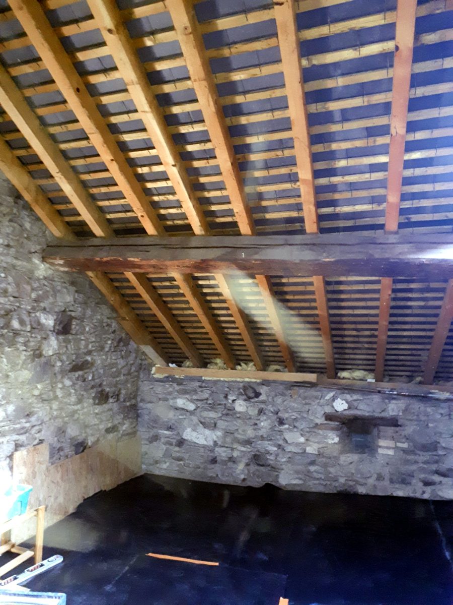 Combles bruts avant travaux : charpente apparente, toiture visible par en-dessous, murs en pierre