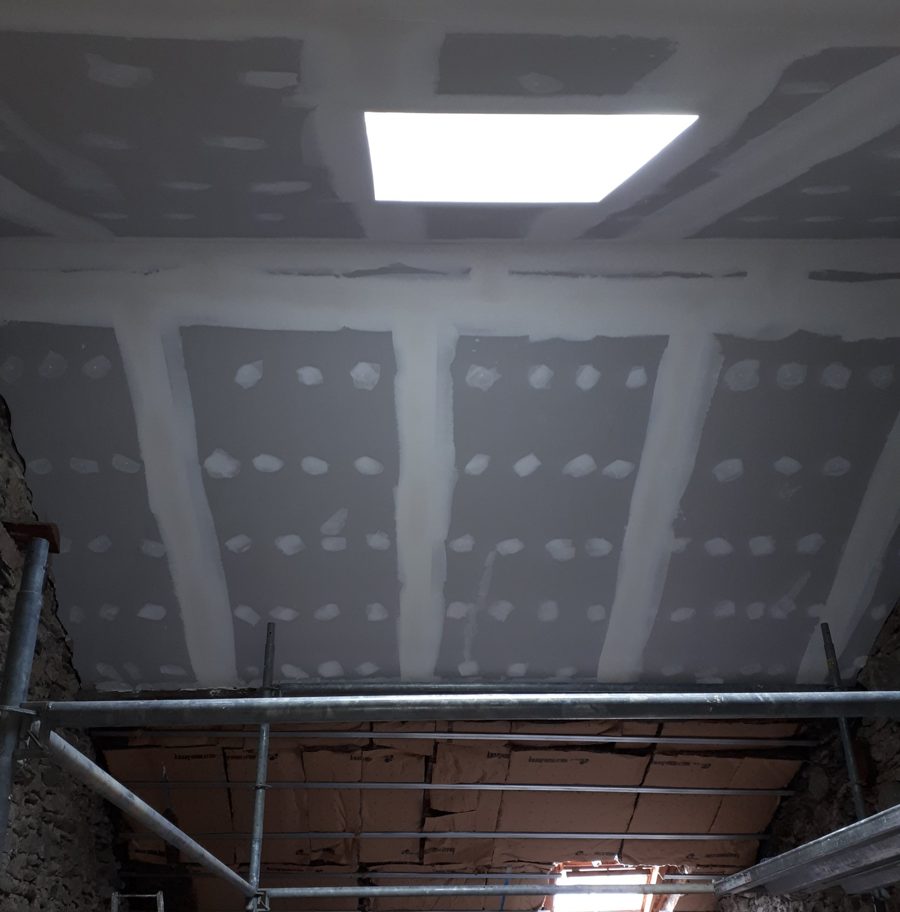 Plaques de plâtre posées sur rampants et plafond, bandes et joints en cours, isolant visible derrière