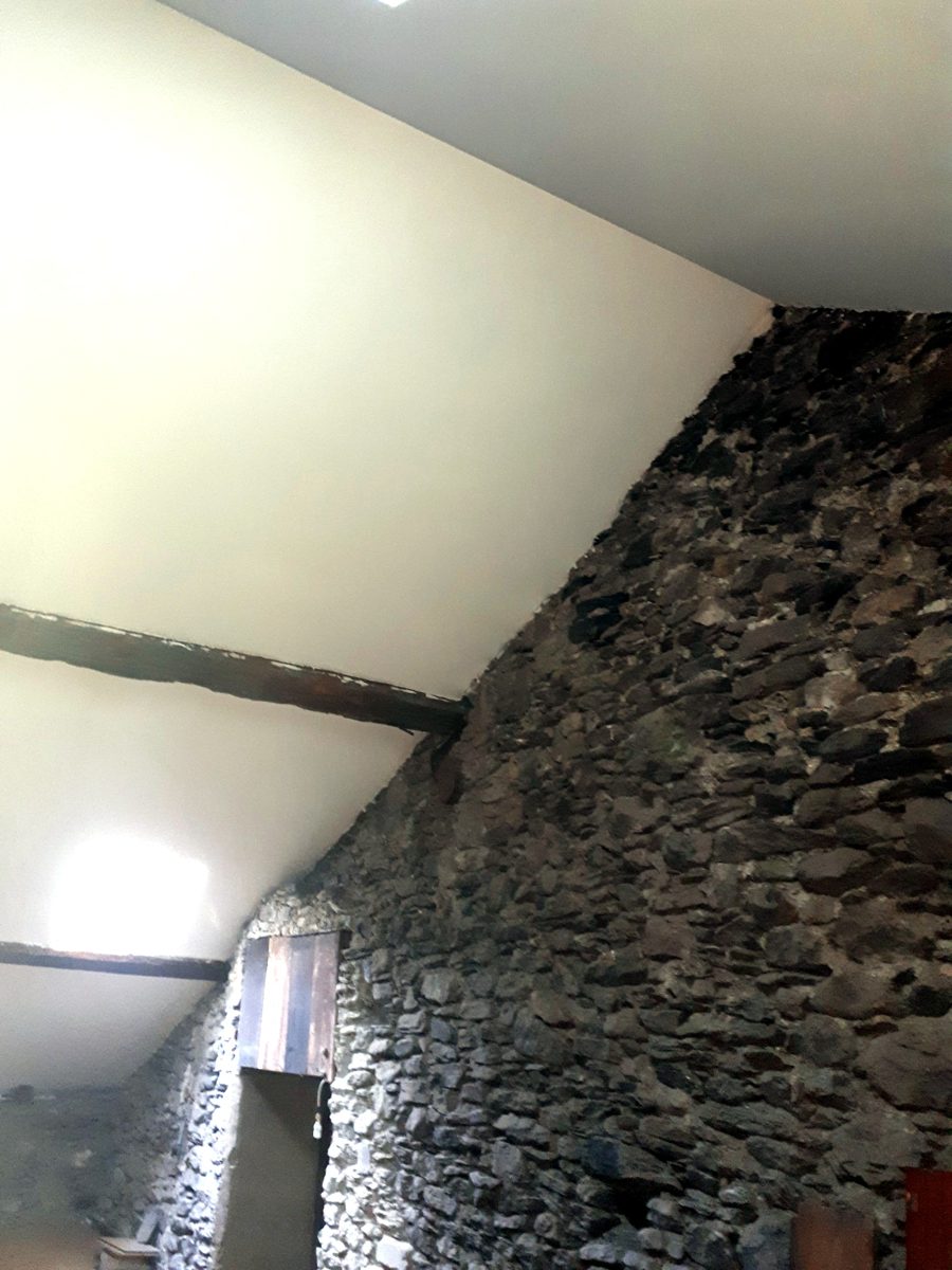 Combles terminés : rampant lisse en plaques de plâtre, poutre ancienne et mur de pierre conservés, fenêtre de toit