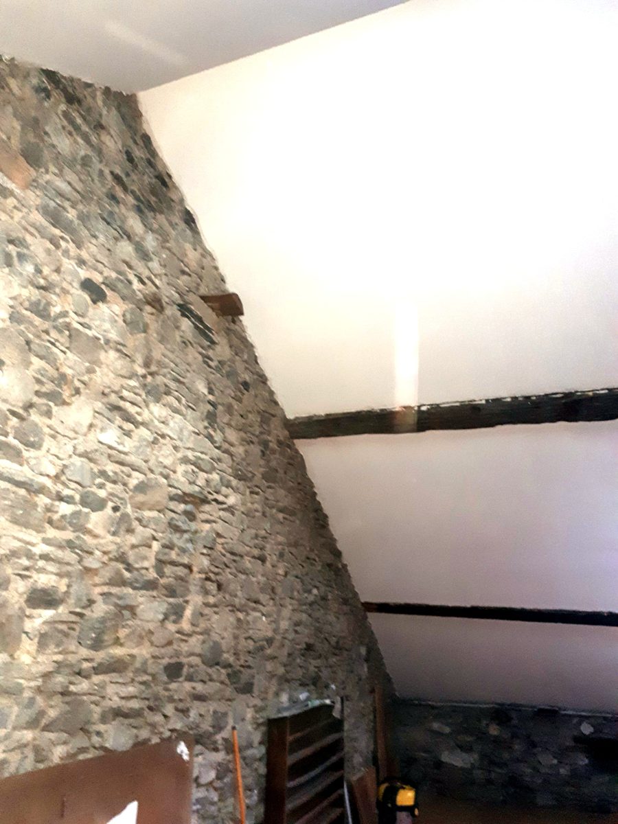 Combles terminés : poutres anciennes conservées entre les surfaces lisses et le mur de pierre